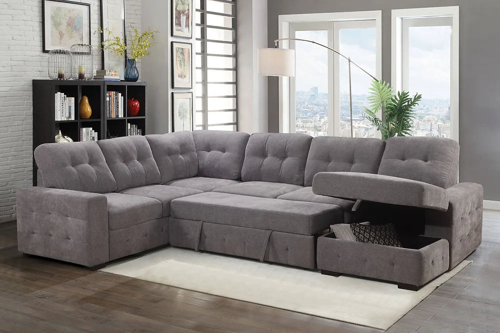 Gray sectional sofa in a living room with a bookshelf and large windows.
